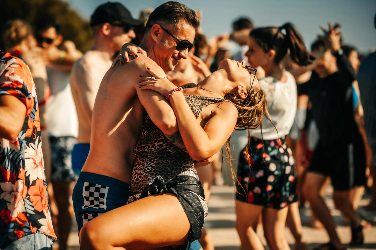 Un cuplu dansând bachata, ea râzând cu capul pe spate, în mijlocul petrecerii
