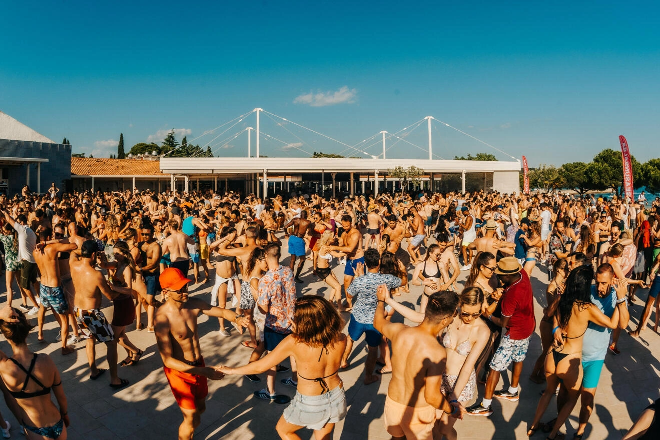 Mulțime de oameni dansând bachata în soare, pe terasa unui festival la malul mării